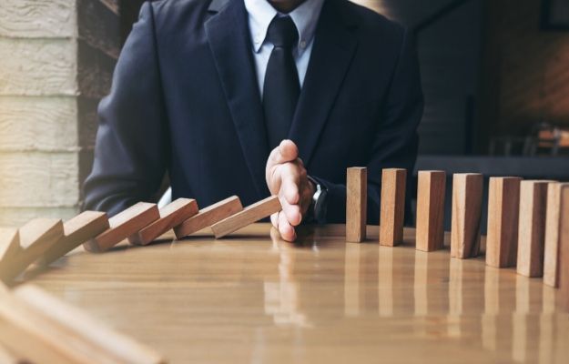 Close up of businessman hand Stopping Falling wooden Dominoes | Risk