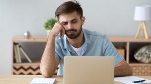 Tired man with note staring at a laptop screen