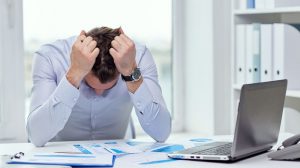 Stressed businessman with papers and charts sitting at table in office