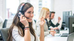 Cheerful young business woman with headphones talking with client in call center