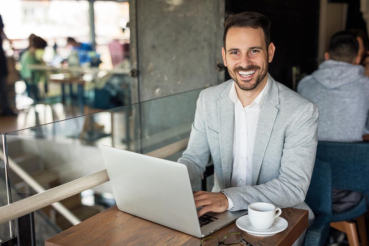 Smiling man using computer in cafe | Essential B2B Marketing Trends That Will Pick Up Steam | B2B digital marketing trends
