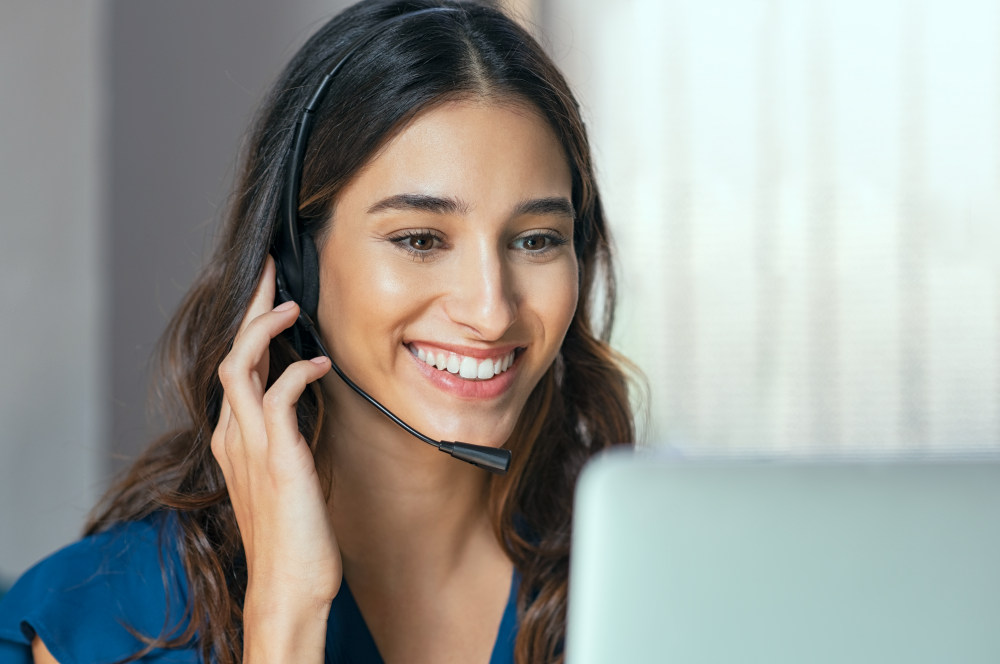 Smiling woman using laptop while talking to customer on phone | How to Master Pre-Call Planning with Jeff Boyle at Cision (PODCAST) | sales call objective