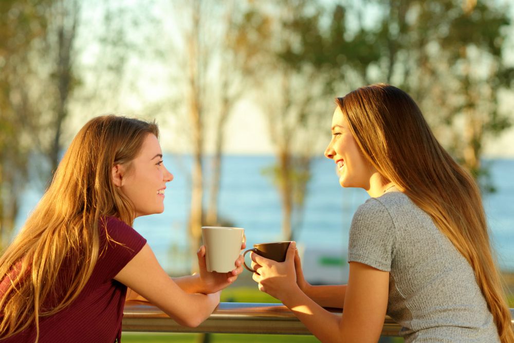 Two happy friends drinking coffee talking outdoors in an apartment balcony by the beach | How To Use The Law of Reciprocity When Social Selling Checklist | feel compelled