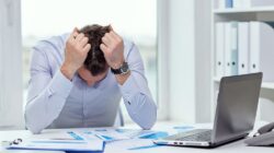 Stressed businessman with papers and charts sitting at table in office